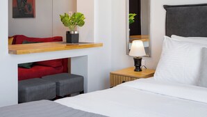 A hotel room with a bed, bedside table, lamp, mirror, artwork, and a plant.
