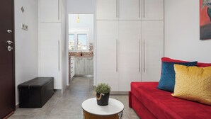 A modern living room with a red sofa, a small round table with a plant, and a view of a kitchen and balcony.