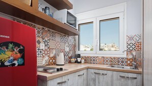 A kitchen with a red refrigerator, patterned tiles, a window, and a view of buildings.