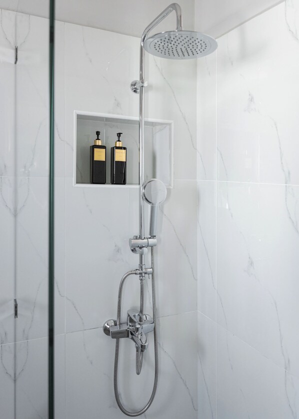 A modern shower with a handheld showerhead and a rain shower attachment. There is a small shelf with two bottles of shampoo and conditioner.