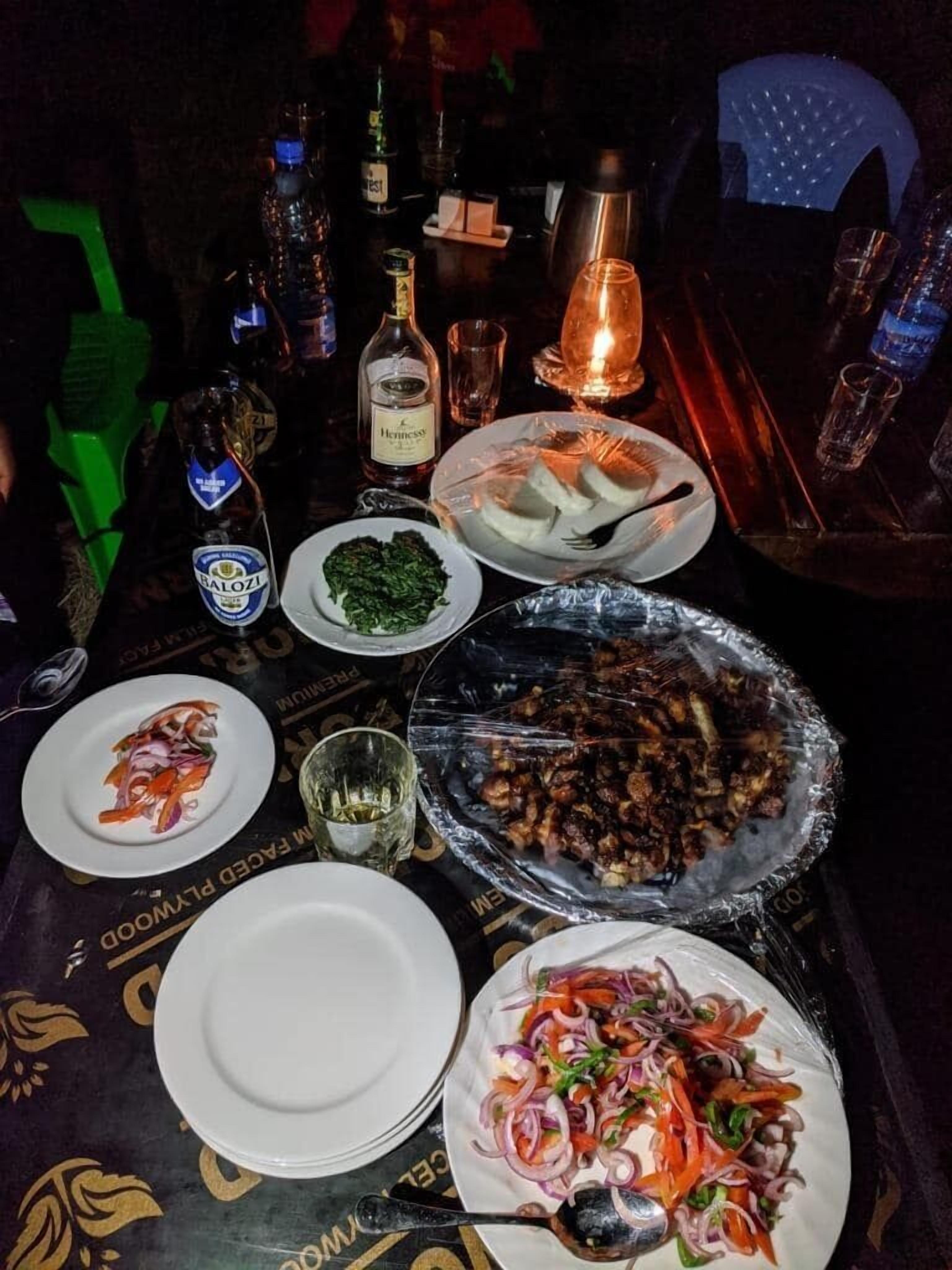 A table set with plates of food, bottles of beverages, and a lit candle.