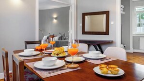 Un comedor con una mesa de madera dispuesta para el desayuno, que incluye croissants, zumo de naranja y bollería.