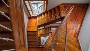 Una escalera en espiral de madera con barandillas metálicas y un tragaluz arriba.