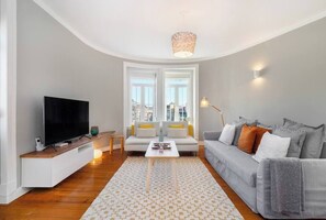 Ein modernes Wohnzimmer mit Flachbildfernseher, einer Couch, einem Couchtisch und einem gemusterten Teppich.