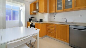 Una cucina moderna con mobili in legno, un piano di lavoro bianco, una lavastoviglie e una finestra che lascia entrare luce naturale.