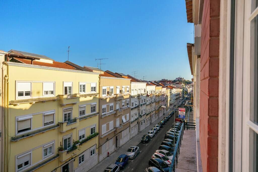 A row of terraced houses with balconies, a clear sky, and parked cars along the street.