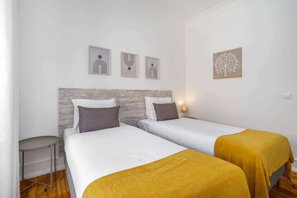 A hotel room with two beds, a small table, and three framed artworks on the wall.