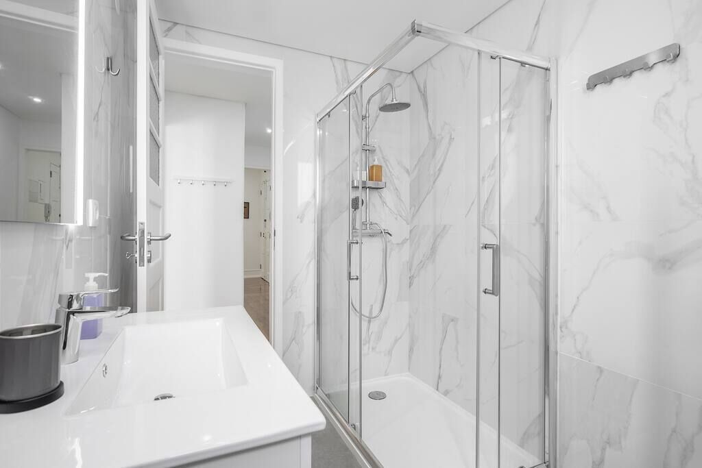 Een moderne badkamer met een witte marmeren wastafel, een douche met glazen wand en een grote spiegel.