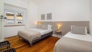 Une chambre avec deux lits, une cuisinière à gaz, une fenêtre avec des stores et deux appliques murales.