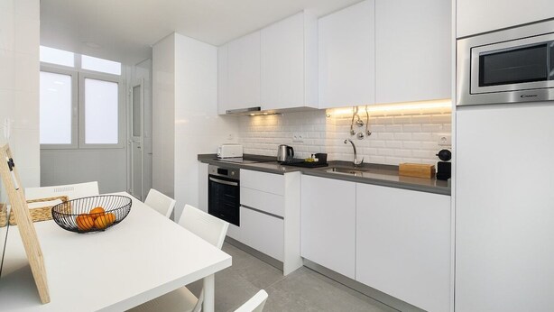 Une cuisine moderne avec des meubles blancs, un four encastré et un coin repas comprenant une table et des chaises blanches.
