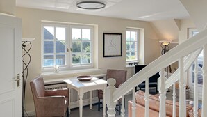 A dining area with a white table and chairs, a window with a view of the outside, and a staircase leading to another level. - Heefwai 2 - W4 - Just completed - upper floor with sensational views (Sylt-Ost)