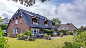 A two-story house with a sloped roof, a brick exterior, and a well-maintained garden with outdoor furniture. - Heefwai 2 - W4 - Just completed - upper floor with sensational views (Sylt-Ost)