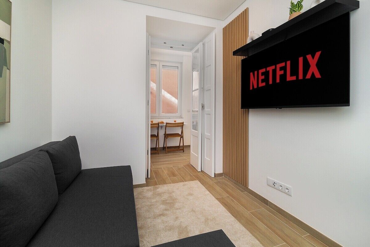 Ein modernes Wohnzimmer mit einem dunkelgrauen Sofa, Holzboden und einem an der Wand befestigten Fernseher, der das Netflix-Logo zeigt.