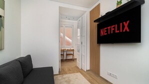 A modern living room with a dark sofa, a wooden floor, and a wall-mounted TV displaying the Netflix logo.