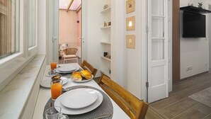 A dining area with a table set for two, a TV mounted on the wall, and a door leading to a balcony.