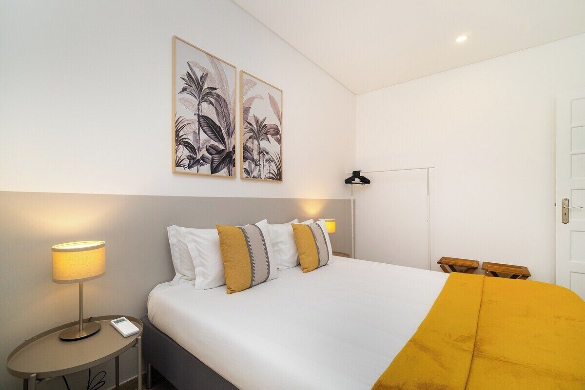 A hotel room with a bed, two bedside lamps, a nightstand, a wall-mounted picture, and a door.