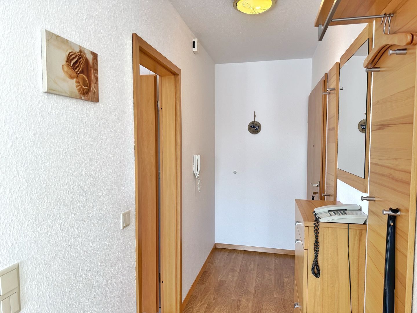 Un couloir avec des portes en bois, un téléphone et un luminaire fixé au mur.