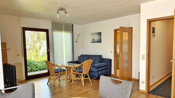 A modern living room with a sofa, two chairs, a small table, and a dining table with a notebook. - Baltique - Holiday apartment 5 Glowe - Holiday apartment Baltique 5 (Glowe)