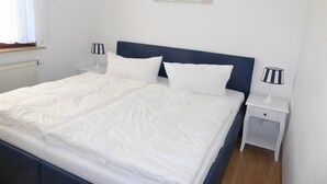 A neatly made bed with white linens, a dark blue headboard, and two bedside tables with lamps. - Baltique - Holiday apartment 5 Glowe - Holiday apartment Baltique 5 (Glowe)