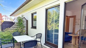 A patio with a table and chairs, a sliding glass door leading to a room, and a view of trees and a neighboring house. - Baltique - Holiday apartment 5 Glowe - Holiday apartment Baltique 5 (Glowe)