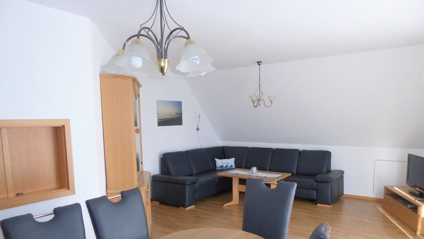 A modern living room with a dark-colored sofa, a wooden dining table with chairs, and a television on a wooden stand. - Baltique - Holiday apartment 7 Glowe - Holiday apartment Baltique 7 (Glowe)
