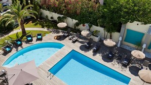 A large outdoor swimming pool with multiple lounge areas and umbrellas, surrounded by greenery and a white wall. - Comfortable Room in Cannes for 2 Guests (Cannes)