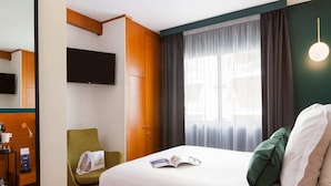 A hotel room with a bed, a green armchair, a TV mounted on the wall, and a window with curtains. - Comfortable Room in Cannes for 2 Guests (Cannes)