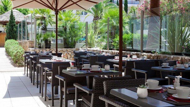 An outdoor dining area with wicker tables and chairs, large umbrellas, and a view of greenery and buildings. - Comfortable Room in Cannes for 2 Guests (Cannes)