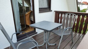 A balcony with a table and two chairs, a wicker basket, and a window with a curtain. - Baltique - Holiday apartment 4 Glowe - Holiday apartment Baltique 4 (Glowe)