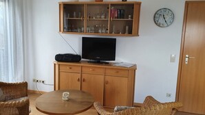 A living room with a wooden cabinet containing glassware, a television, and a clock on the wall. - Baltique - Holiday apartment 4 Glowe - Holiday apartment Baltique 4 (Glowe)