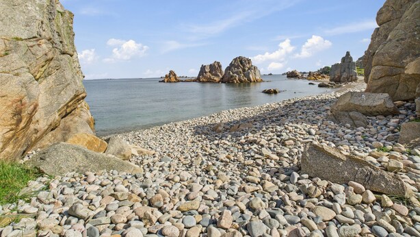 Une plage rocheuse parsemée de gros blocs de pierre, offrant une vue dégagée sur la mer.
