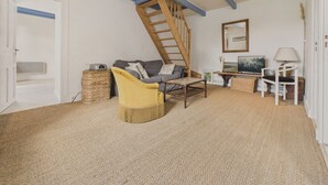 Un salon chaleureux avec un plafond haut, un escalier en bois, un canapé, un fauteuil jaune, une petite table, une lampe et un tableau accroché au mur.