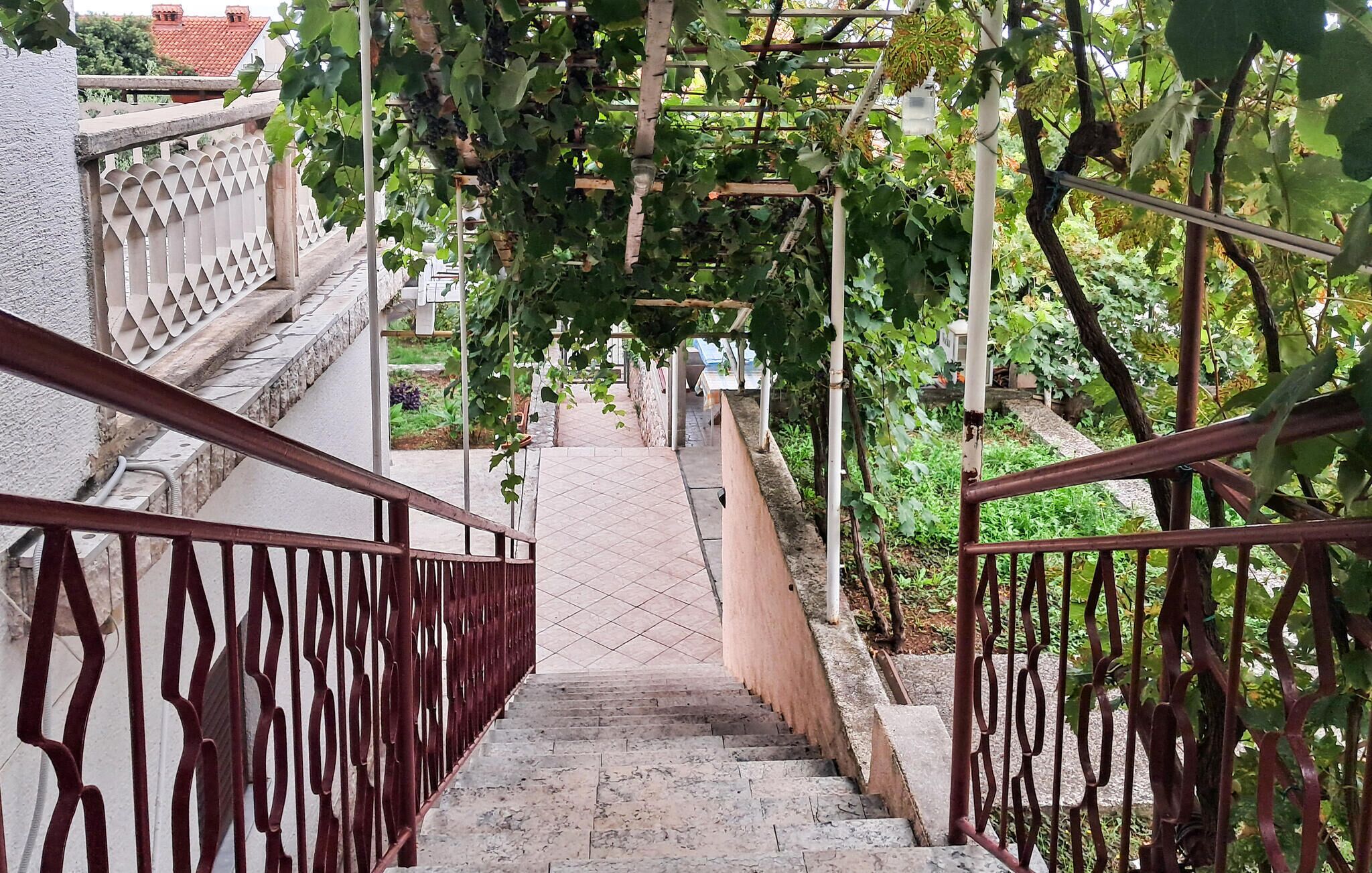 Eine Treppe mit Metallgeländern, umgeben von Grünpflanzen und einem gefliesten Weg.