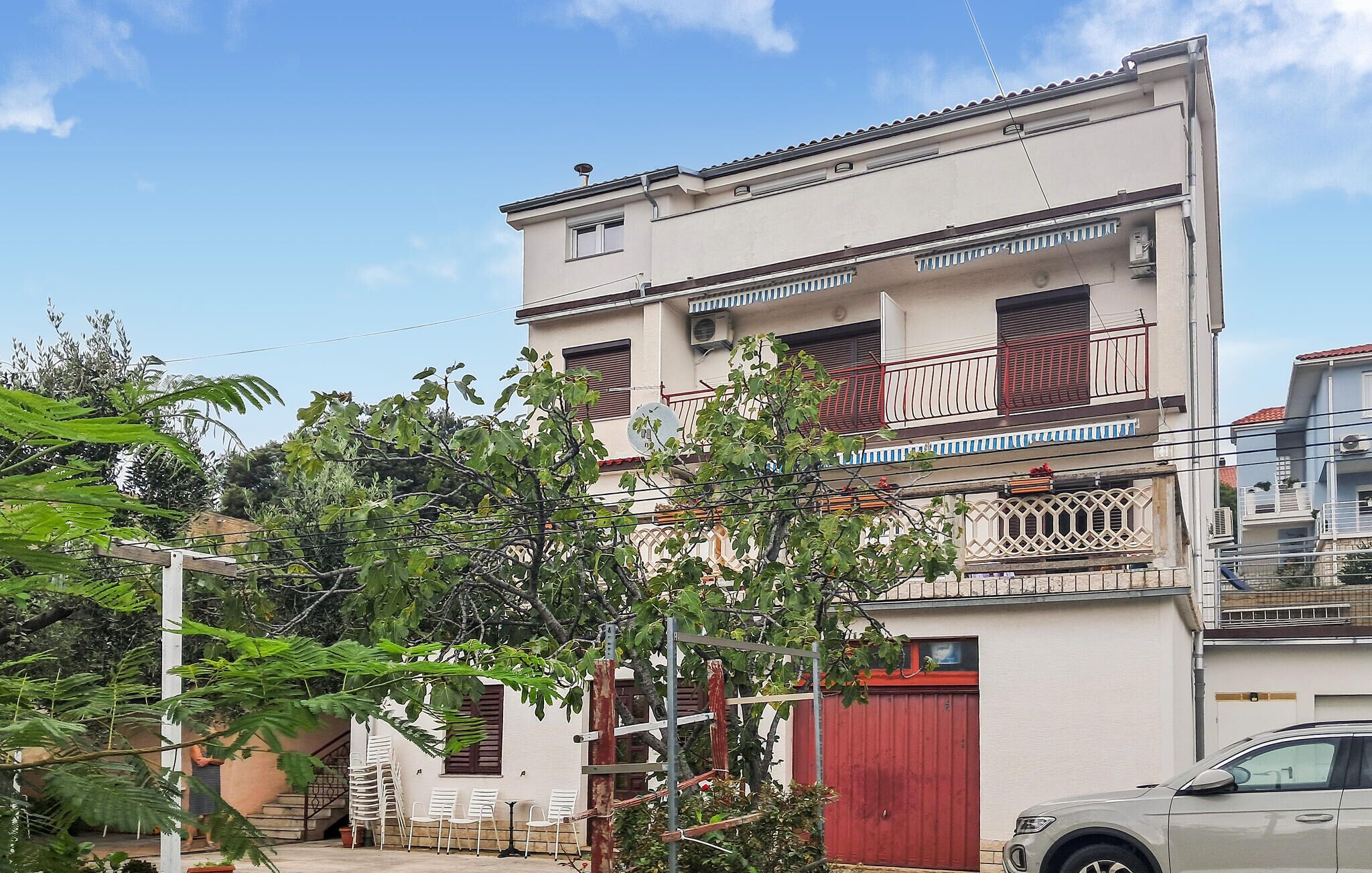 Un edificio de varios pisos con balcones, una puerta de garaje roja y mobiliario exterior.
