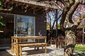 A wooden deck with a table and bench, a glass door leading to a room, and a tree with pink blossoms. - Charming Central Stay - Cosy Comfort and Free Parking (Christchurch)