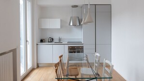 Une cuisine moderne avec des meubles blancs, une table à manger en verre et des luminaires suspendus.