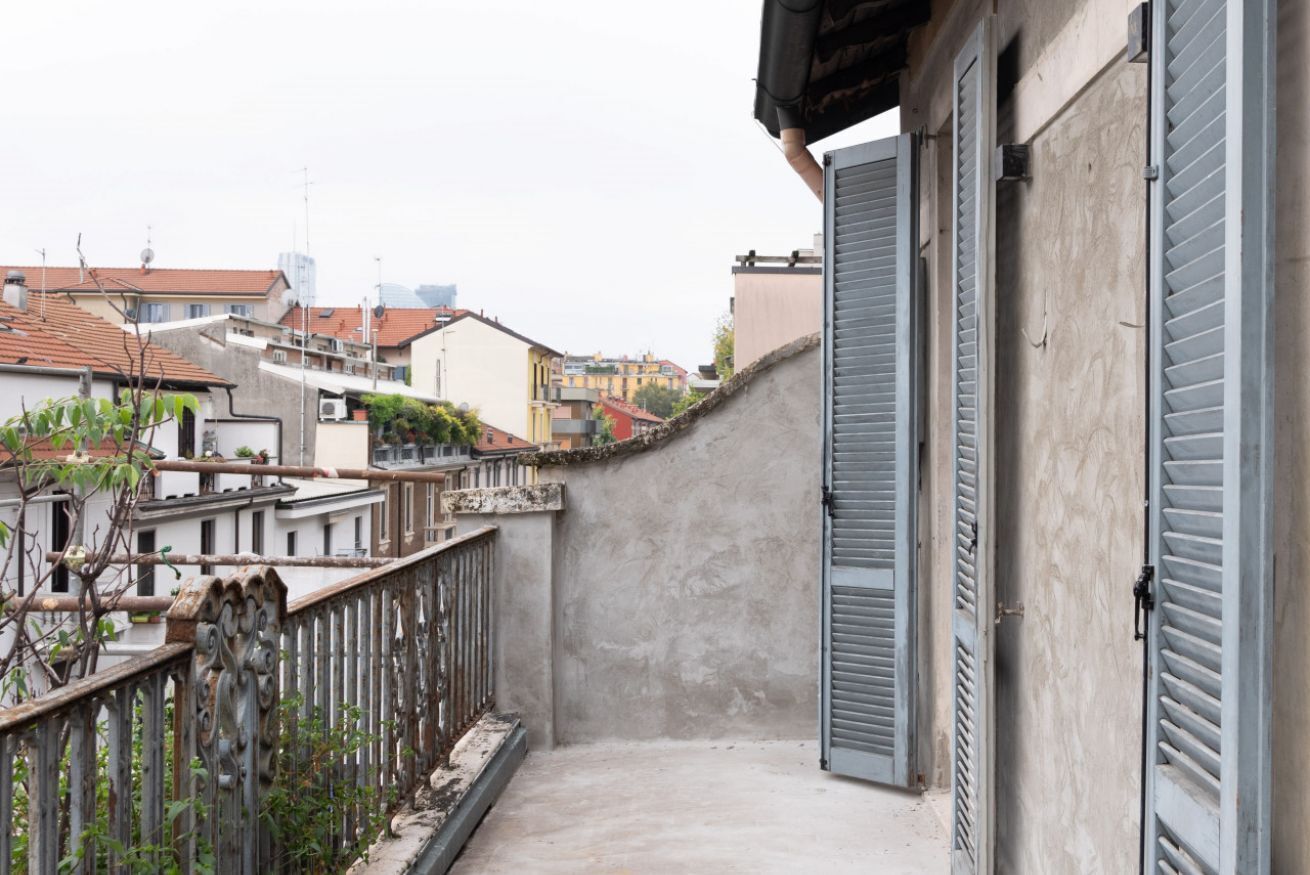 A narrow balcony with a concrete floor, metal railing, and closed shutters.