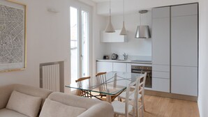 Une cuisine moderne avec une table à manger en verre, des meubles blancs et des luminaires suspendus.