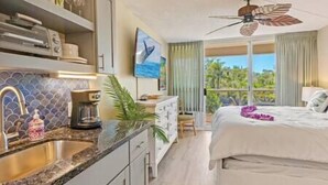 A hotel room with a bed, a ceiling fan, a coffee maker, a sink, and a window with a view of greenery. - Maui Banyan Studio, King Bed, Steps to Kam2 Beach (Kihei)