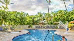 A swimming pool with a tiled deck, surrounded by lush greenery and palm trees. - Maui Banyan Studio, King Bed, Steps to Kam2 Beach (Kihei)