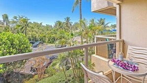 A balcony with a table and chairs, overlooking a tropical landscape with palm trees and a clear sky. - Maui Banyan Studio, King Bed, Steps to Kam2 Beach (Kihei)