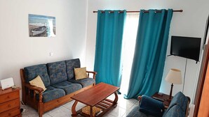 A living room with a sofa, a wooden coffee table, a TV, and teal curtains.