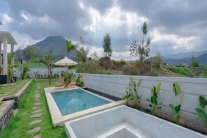A swimming pool with a stone pathway leading to it, surrounded by greenery and a white wall. - RedDoorz @ Volcano Mountain View Kintamani (Bali)