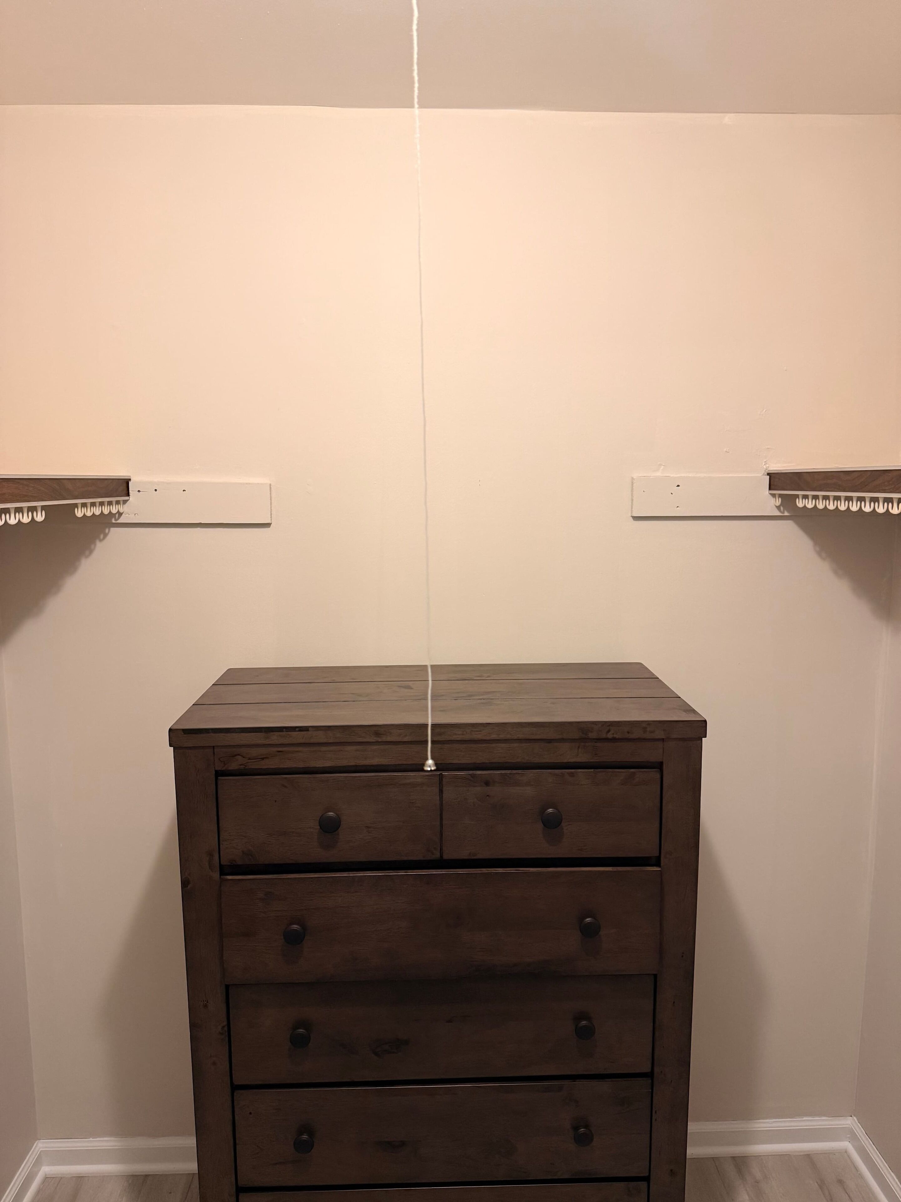 Eine hölzerne Kommode mit Schubladen vor einer schlichten Wand, daneben zwei weiße Regale.