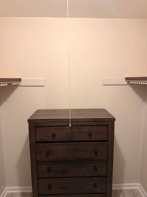 Eine hölzerne Kommode mit Schubladen vor einer schlichten Wand, daneben zwei weiße Regale.