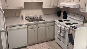 Una cocina con armarios blancos, horno empotrado, lavavajillas y suelo de madera claro.