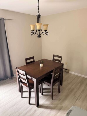 Un coin repas avec une table et des chaises en bois, un lustre suspendu et une plante posée sur la table.