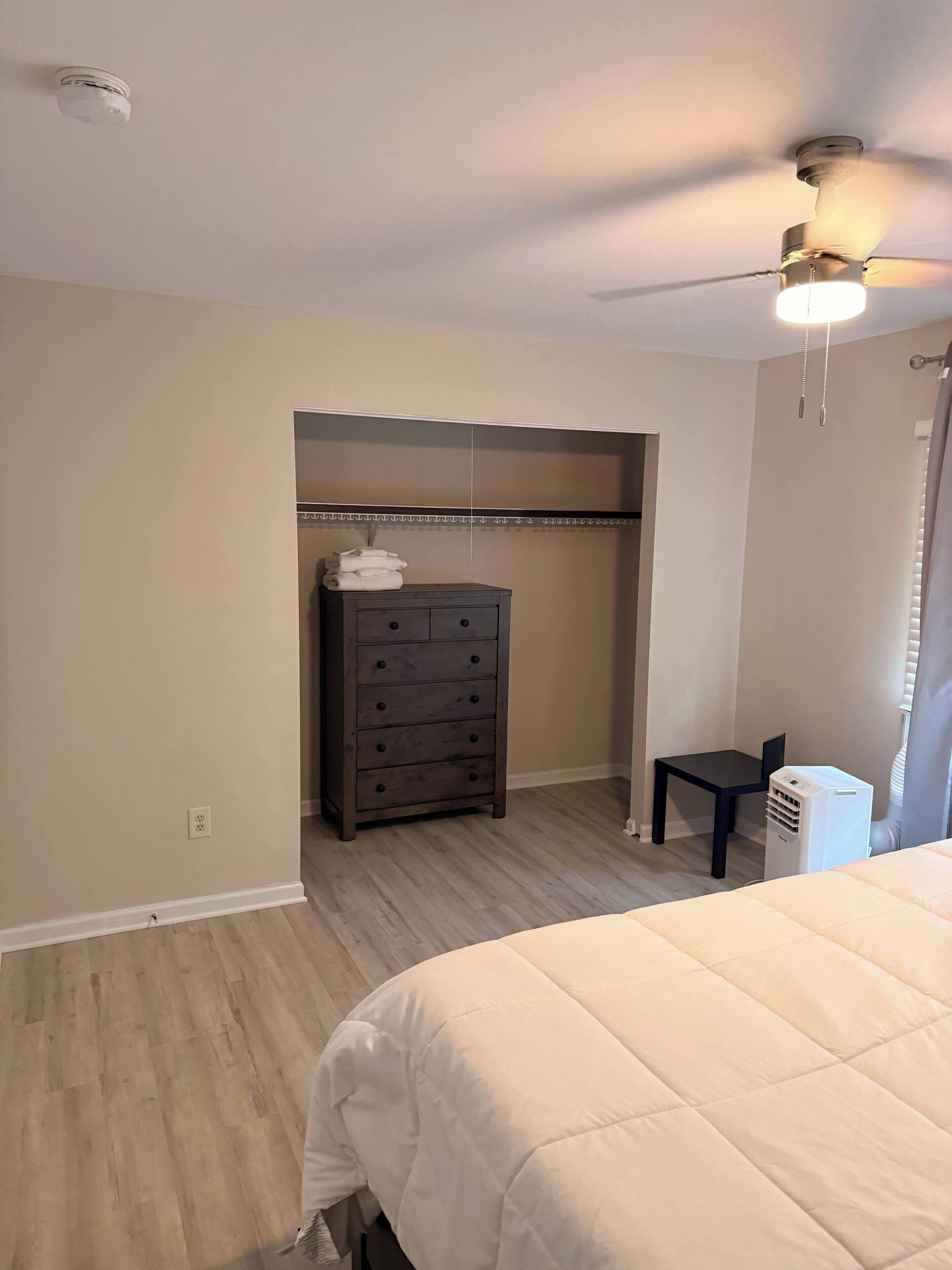 Quarto com cama, penteadeira, cadeira, ventoinha no teto e ar condicionado.