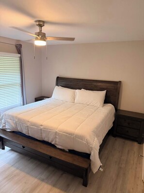 Une chambre à coucher avec un lit, une tête de lit en bois, une table de chevet, un banc et un ventilateur de plafond.