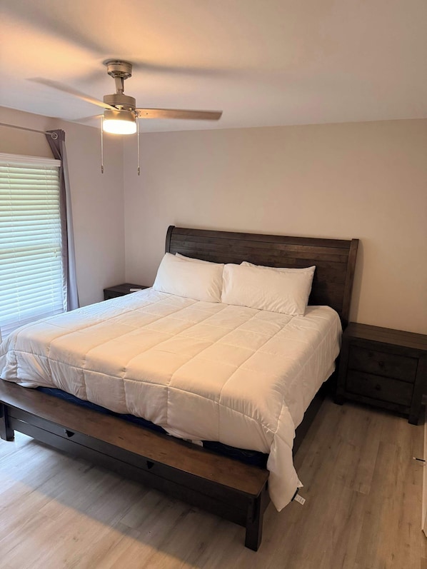 A bedroom with a bed, a wooden headboard, a nightstand, a bench, and a ceiling fan.